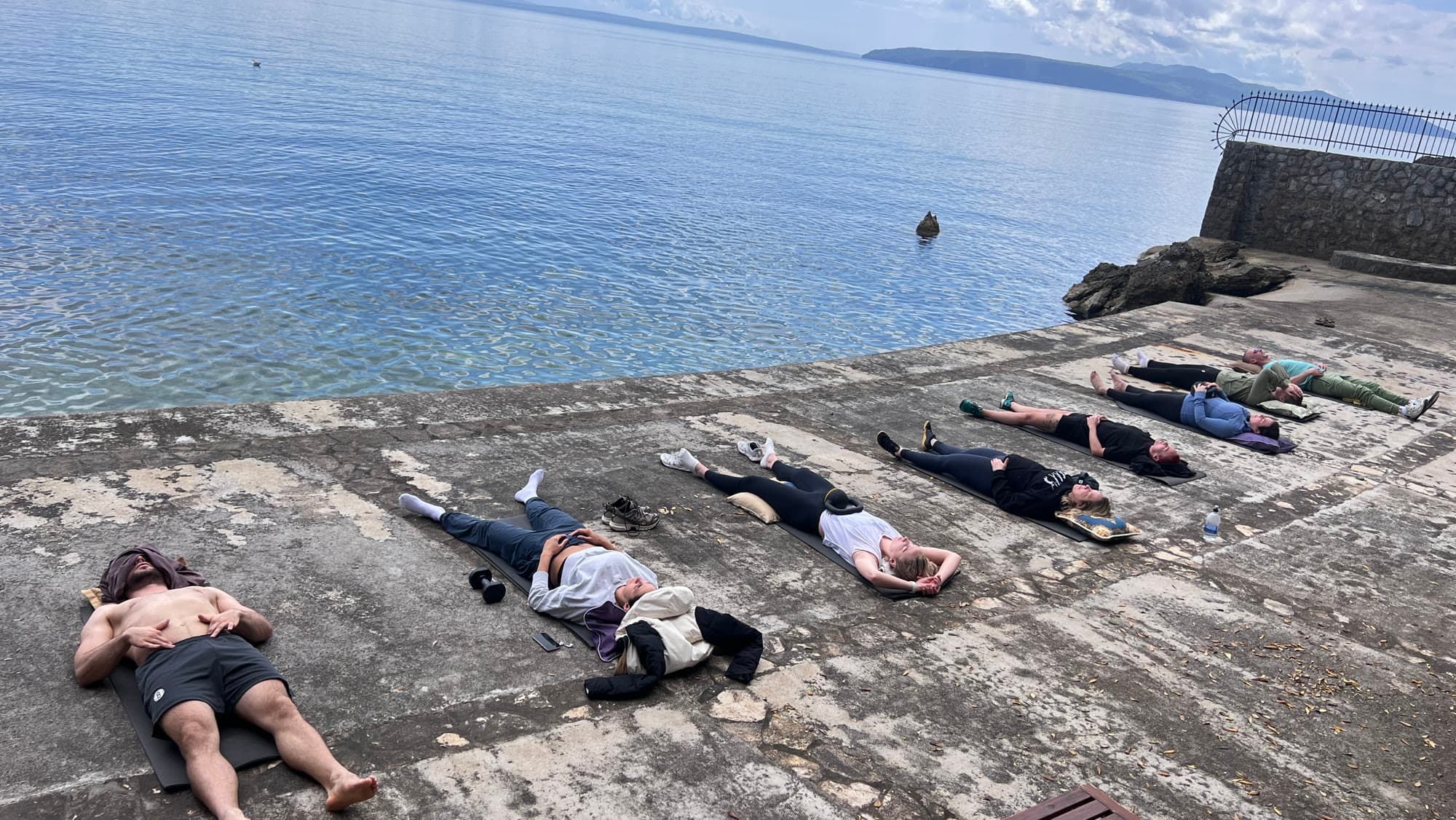 People lying on a weathered terrace beside the sea, attention on breath.