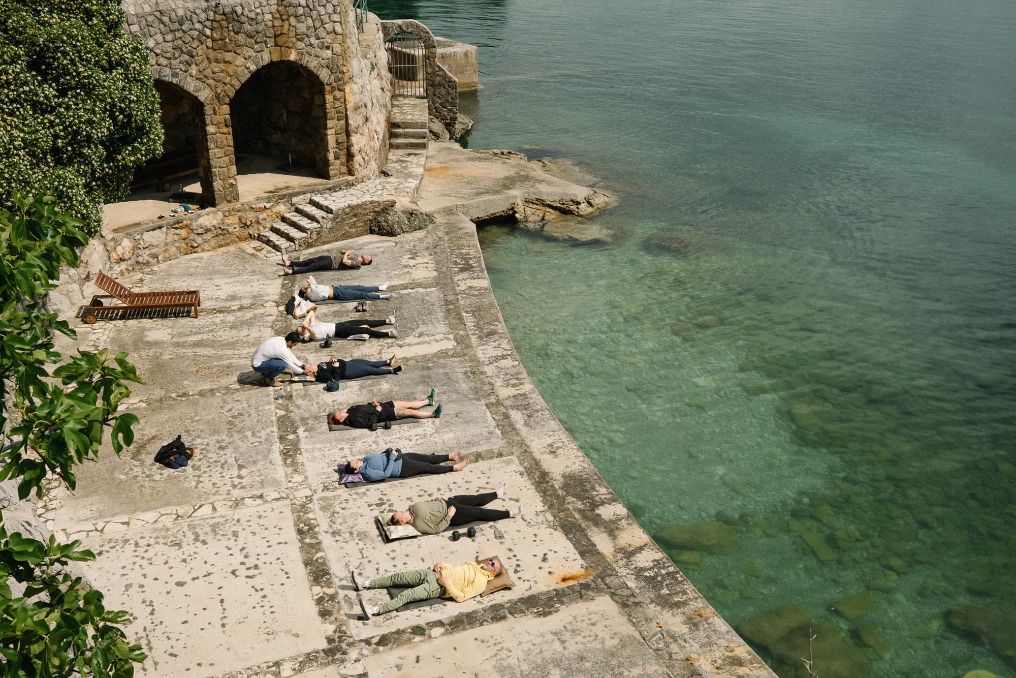 A facilitator kneeling beside a participant during a breath session by the water.
