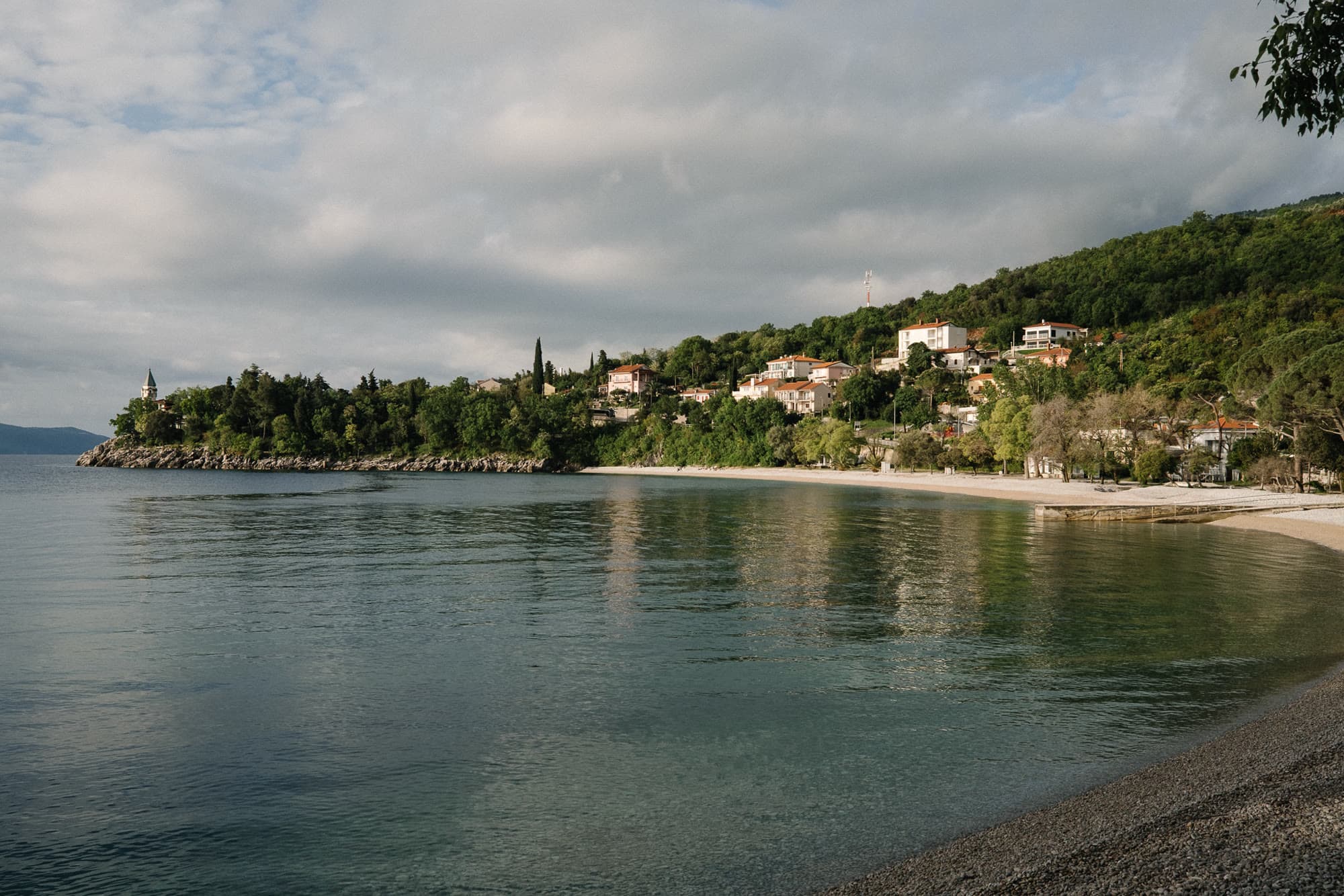 A quiet bay, pebble shore, and hillside houses.