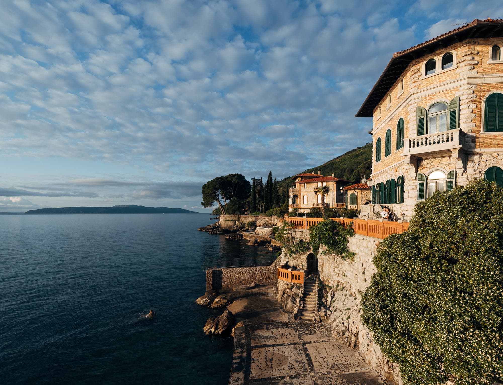 A stone villa on a rocky coastline, the setting for the work.