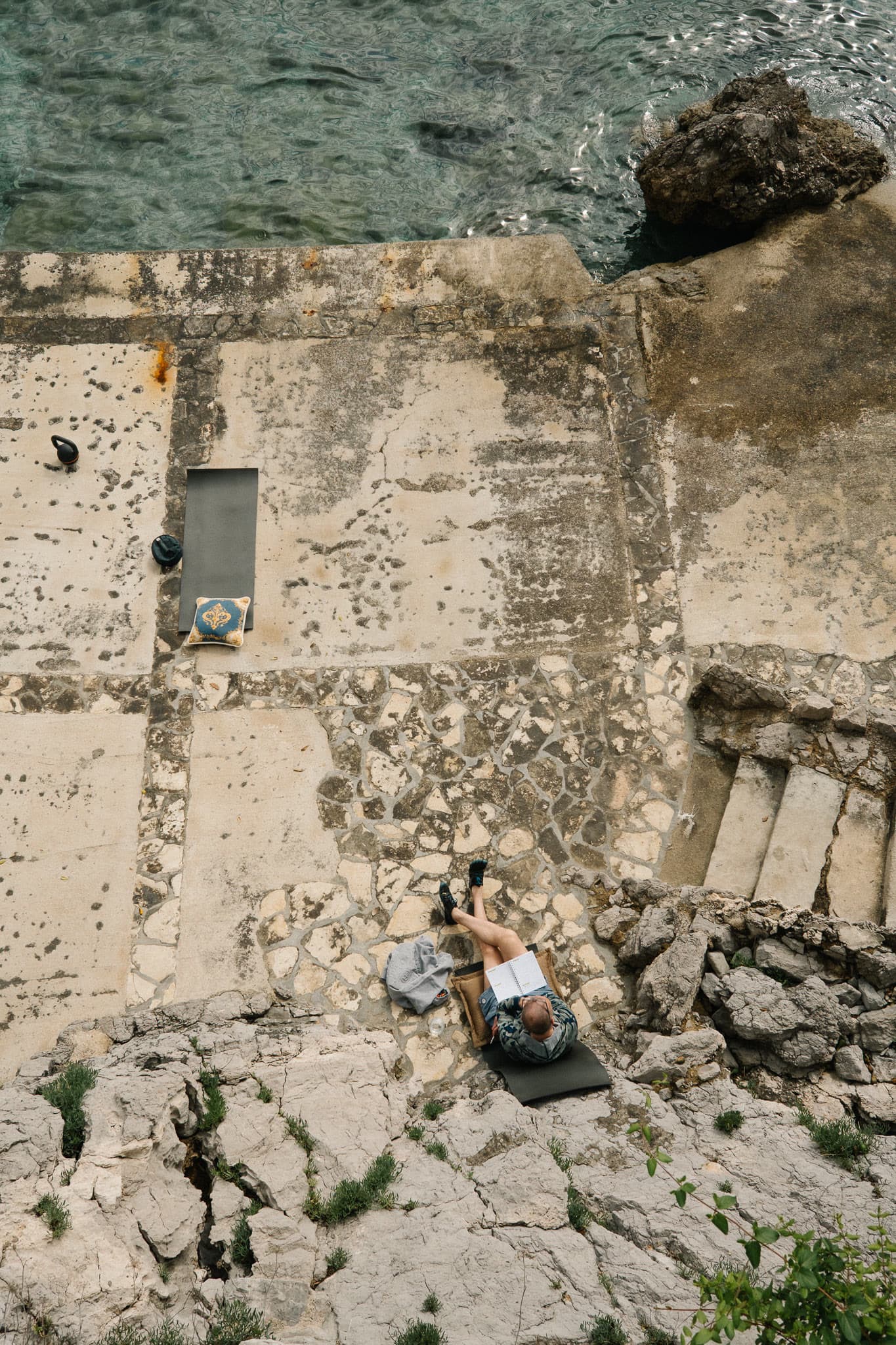 A person sitting on a stone terrace with a notebook, after physical work.
