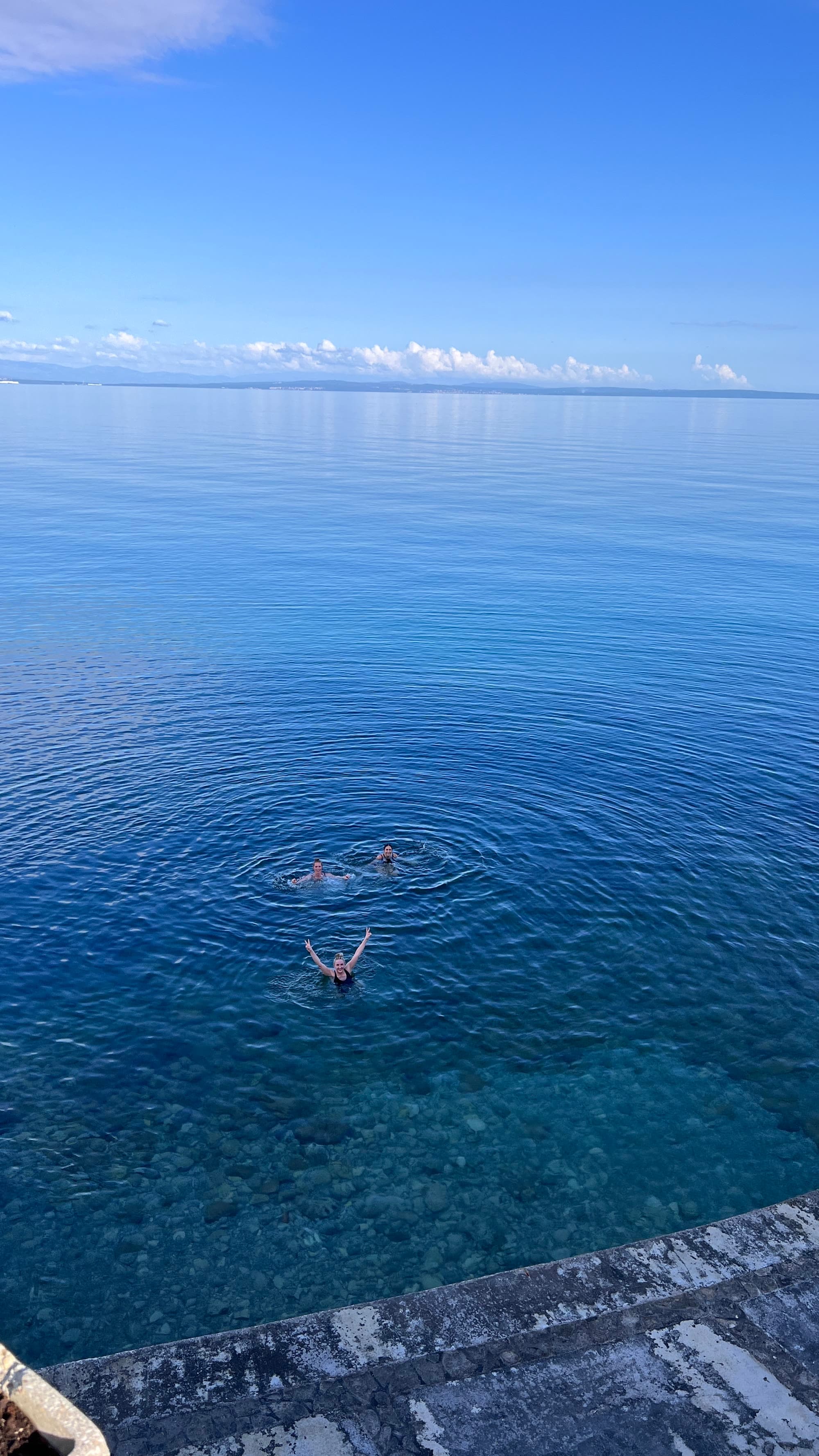 Open water, three swimmers, one looking up with arms raised.